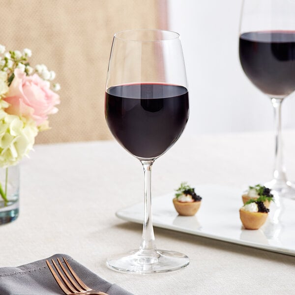 A table set with Acopa Covella wine glasses, wine, and flowers.