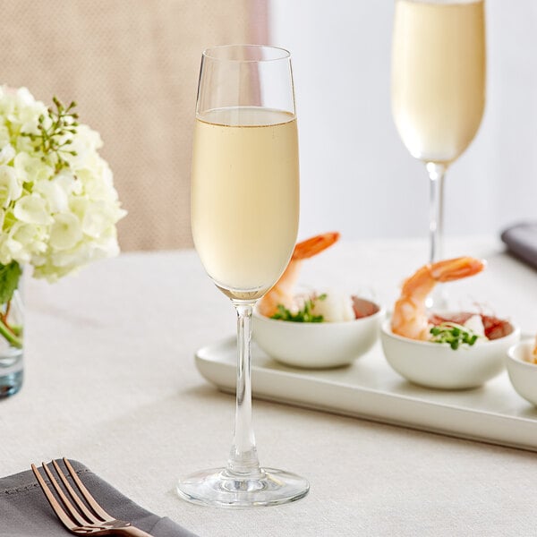 Two Acopa Covella flute glasses of champagne on a table with shrimp.