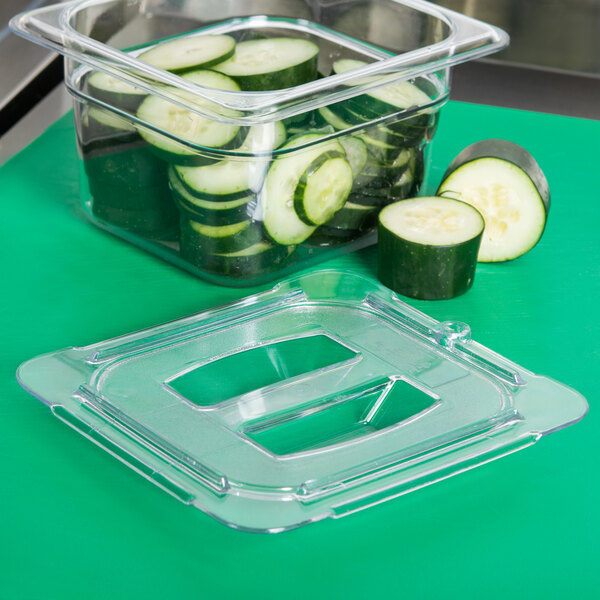 A Carlisle clear plastic container lid on a container of cucumbers and cucumber slices.