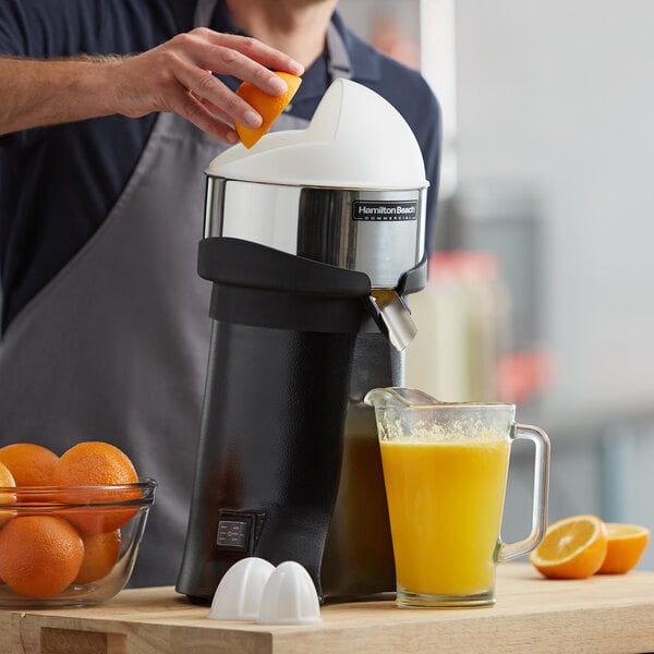 A person squeezing an orange into a Hamilton commercial juicer on a counter with a bowl of oranges.