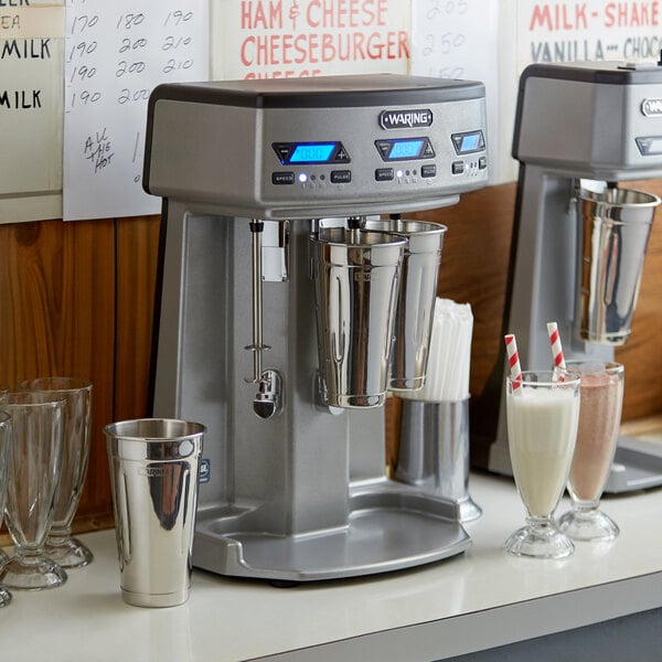 A Waring triple spindle drink mixer on a counter with glasses and cups.