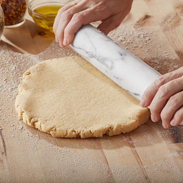 A person rolling out Bob's Red Mill gluten-free pizza crust dough on a table with a rolling pin.
