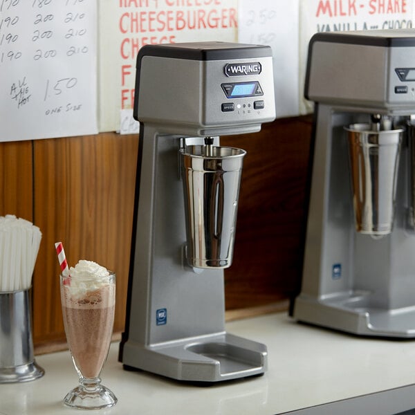 A Waring drink mixer on a counter with a milkshake in a metal cup.