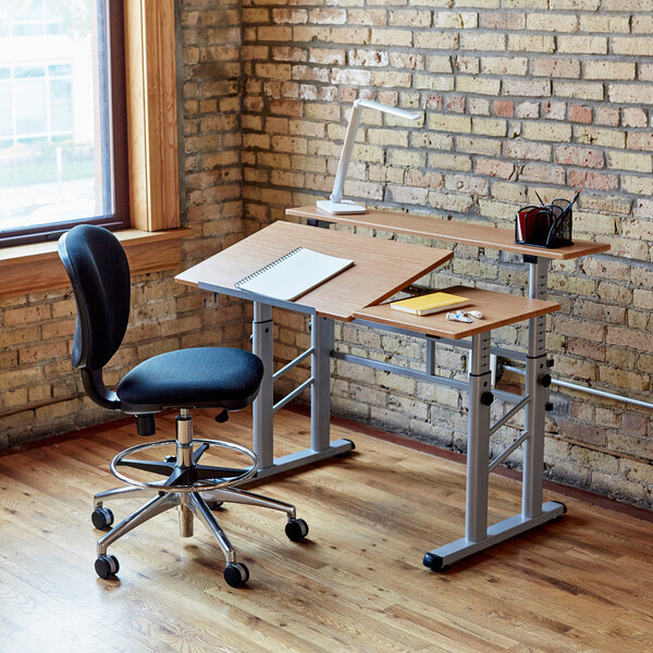 A Safco Medium Oak drafting table with a chair and a notebook on it.