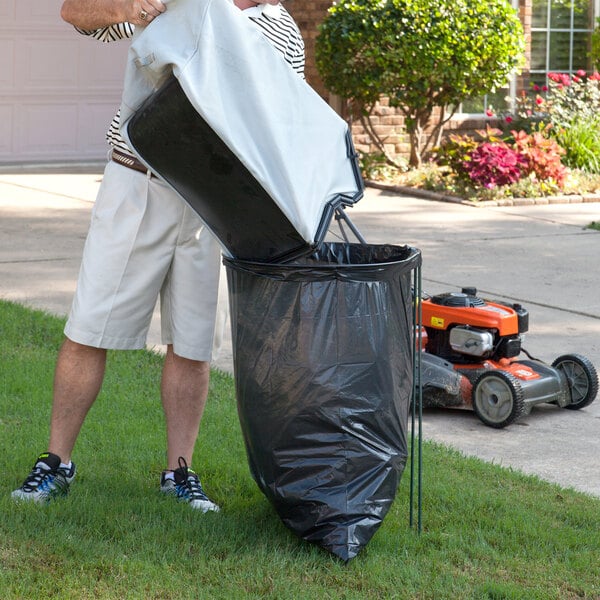 A man using a DeVault EZ Bagger to put a trash bag into a trash can.