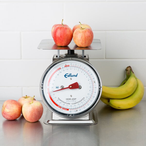 A stainless steel Edlund portion scale on a table with apples on it.