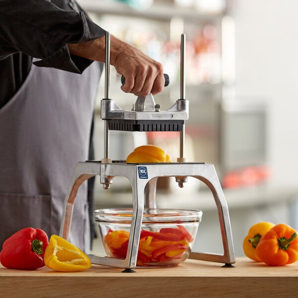 A person using a Vollrath vegetable slicer to cut yellow and orange bell peppers.