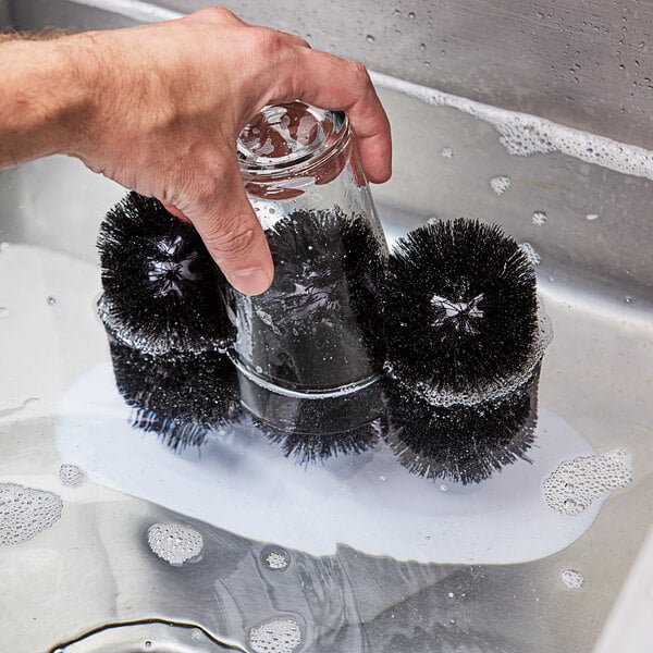 A hand holding a Noble Products Last Call Triple Bar Glass Washer brush in a glass in a sink.