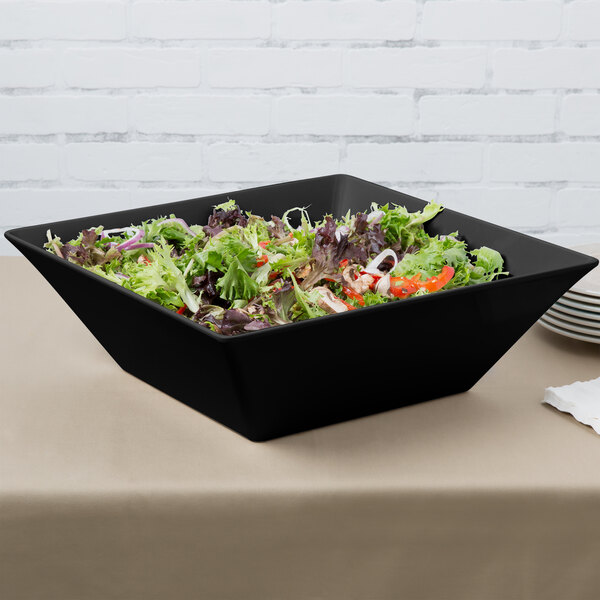 A black GET Siciliano square bowl filled with salad on a table.