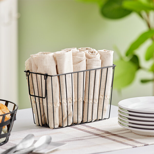 A metal rectangular basket with swinging handles holding napkins and plates on a white table.