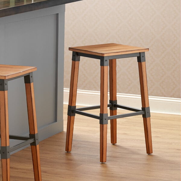 Two Lancaster Table & Seating Rustic Industrial Backless Bar Stools with wood frames sitting on a kitchen counter.