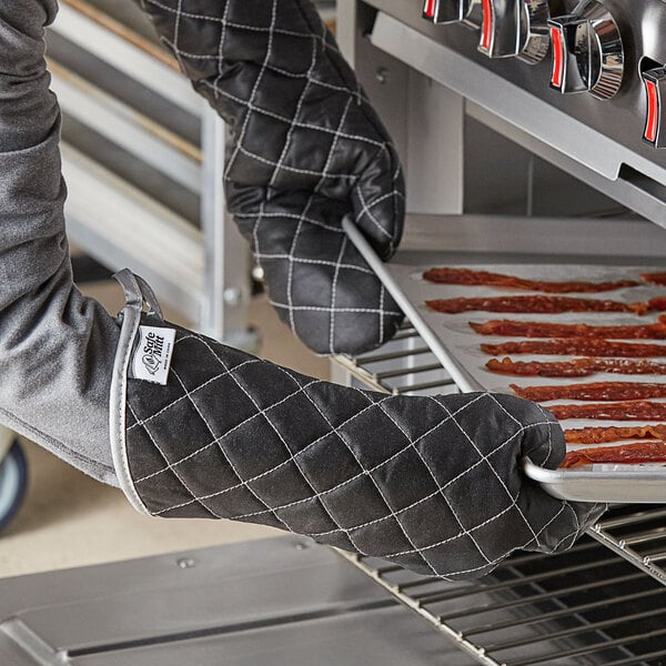 A person using a SafeMitt oven mitt to take a tray of bacon out of an oven.