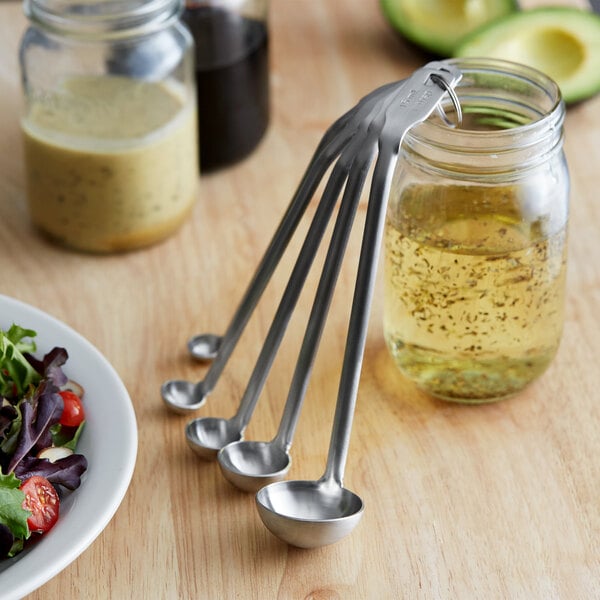 A Vollrath stainless steel measuring spoon set on a table with a bowl of salad.
