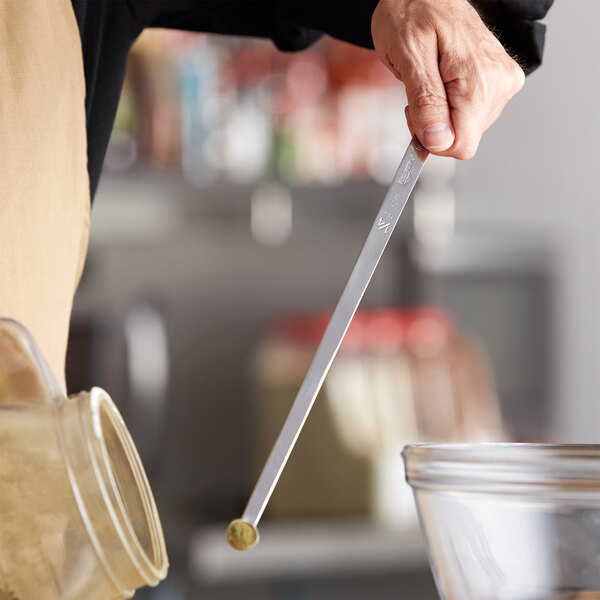 A person using a Vollrath stainless steel long handled measuring spoon to stir something in a bowl.
