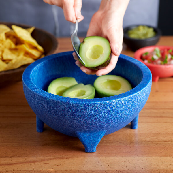 A person using a Choice Thermal Plastic blue Molcajete bowl to cut up an avocado.