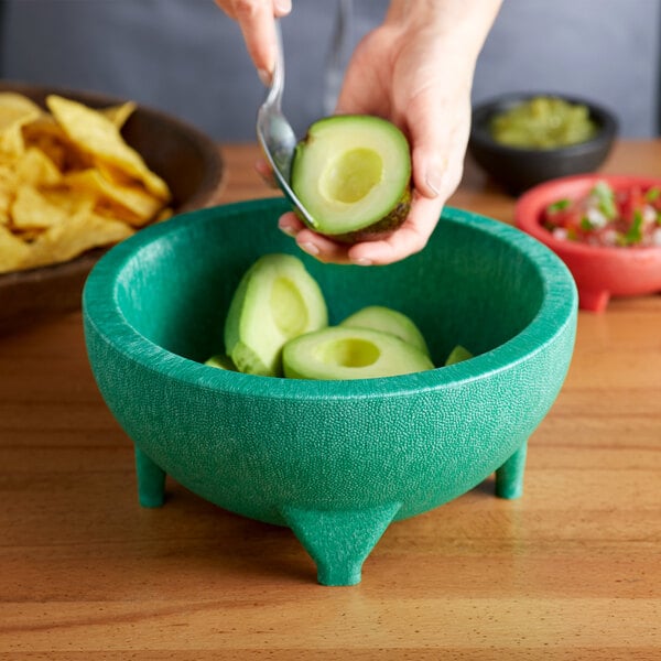 A hand holding a half of avocado peeling into a green Choice Thermal Plastic molcajete bowl.