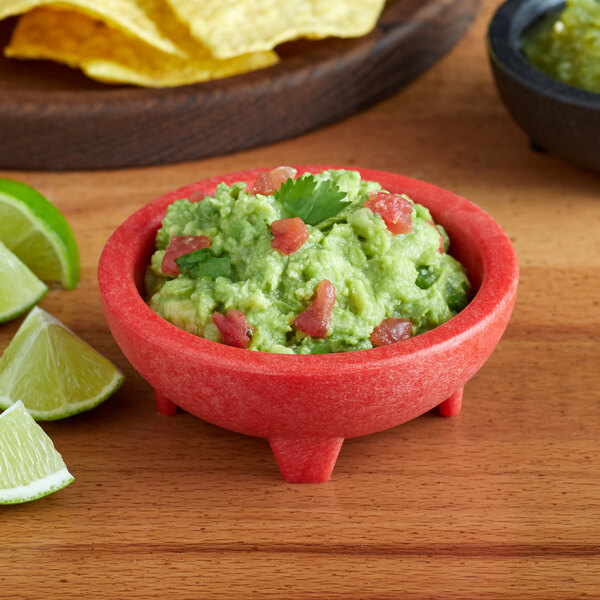A red Choice Thermal Plastic molcajete bowl filled with guacamole and lime slices on a table.