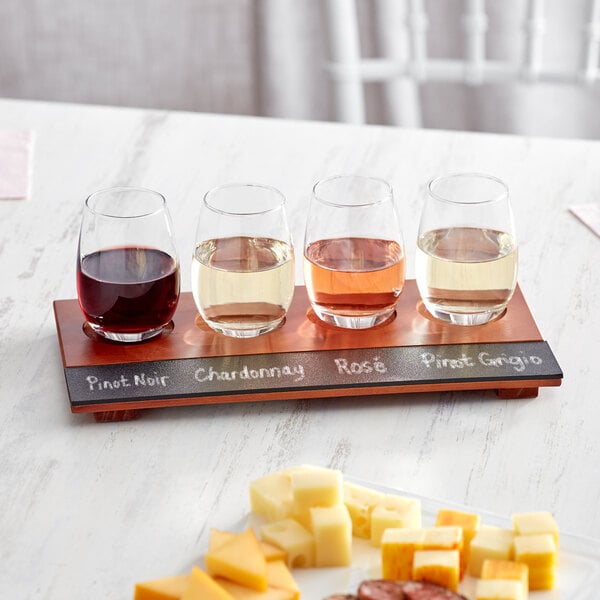 An Acopa Write-On flight tray with stemless wine tasting glasses filled with white, pink, and red wine on a table with cheese and crackers.