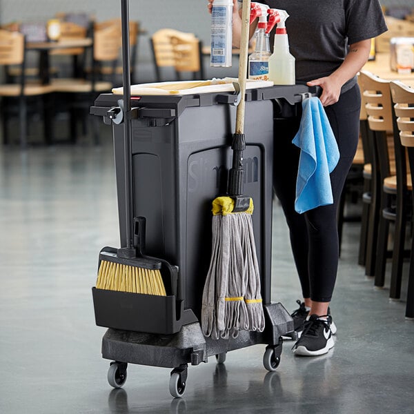 A woman using a Rubbermaid Slim Jim trash container and rim caddy to clean a restaurant