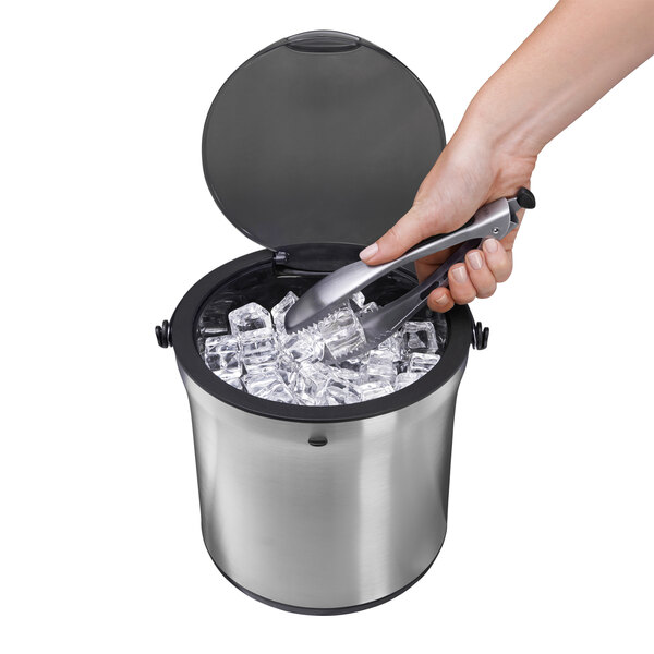 A person using OXO tongs to pick up ice cubes from a stainless steel OXO ice bucket.