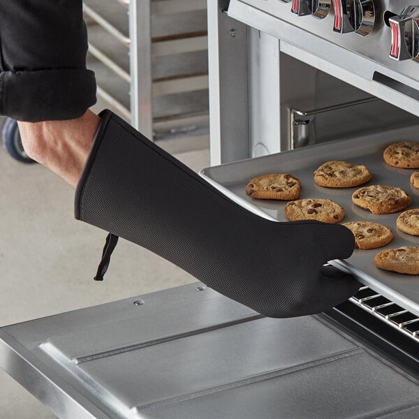 A person using SafeMitt neoprene oven mitts to take a tray of cookies out of an oven.
