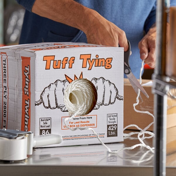 A hand cutting a white box of 3-ply polypropylene industrial twine with scissors.