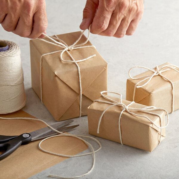 A person tying a string on a brown package with Choice #16 Butcher Sausage Twine