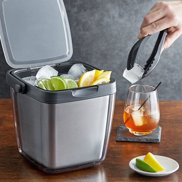 A person using OXO tongs to add lemons to a silver ice bucket.