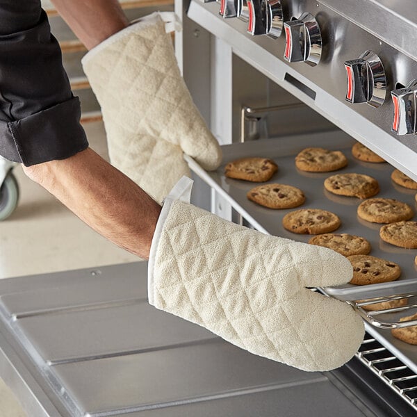 A person wearing Choice terry oven mitts puts a baking sheet of cookies into an oven.