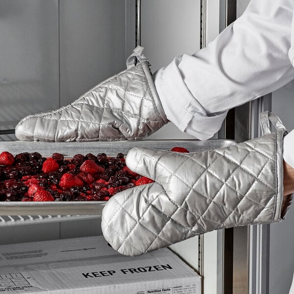 A person wearing Choice silicone oven mitts holding a tray of berries.