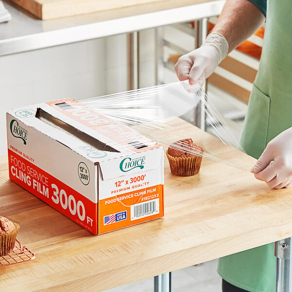 A person in a white apron using Choice Foodservice Film to wrap a box of food.