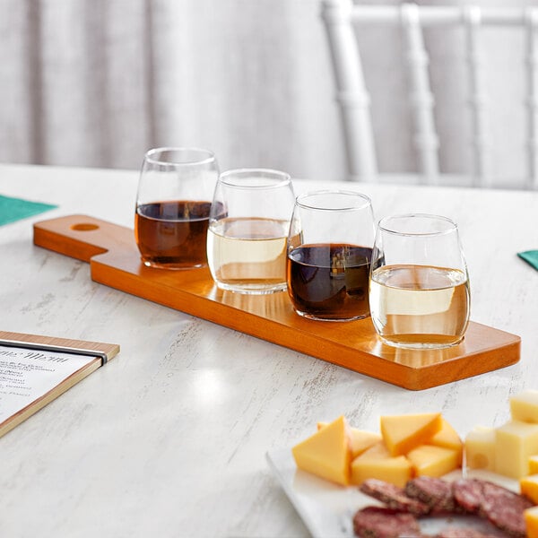 An Acopa dual-sided wooden flight paddle with four stemless wine tasting glasses filled with red and white wine on a table.