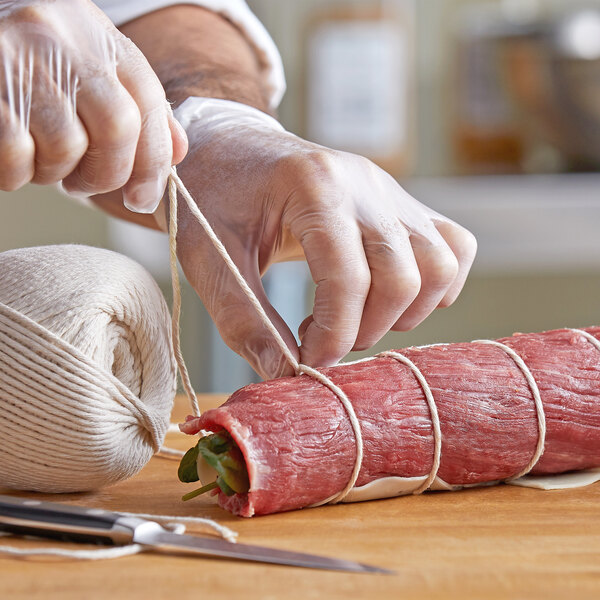 A person in gloves tying Choice Butcher Sausage Twine on a roll of meat.