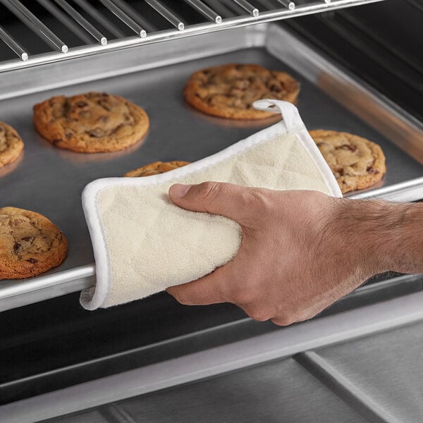 A hand holding a white Choice terry cloth square over a tray of cookies.