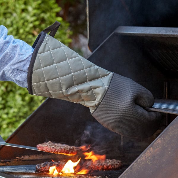 A hand wearing a SafeMitt oven glove using a grill.