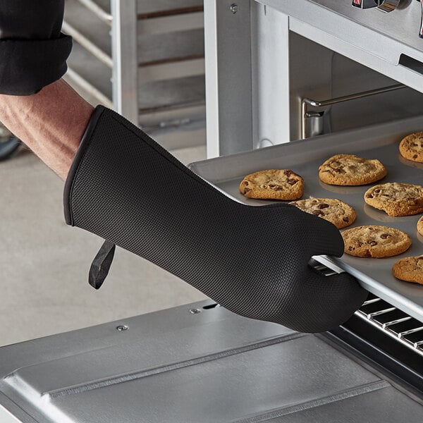 A person wearing a SafeMitt oven glove taking a tray of cookies out of an oven.