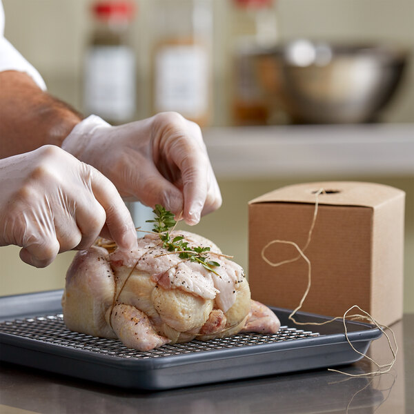 A person in gloves using Choice 4-Ply Linen Sausage Twine to tie herbs on a piece of chicken.