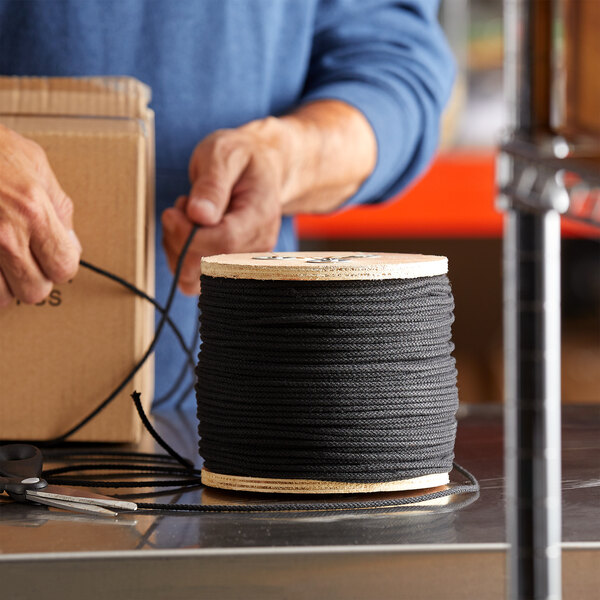 A hand tying black twine to a spool.
