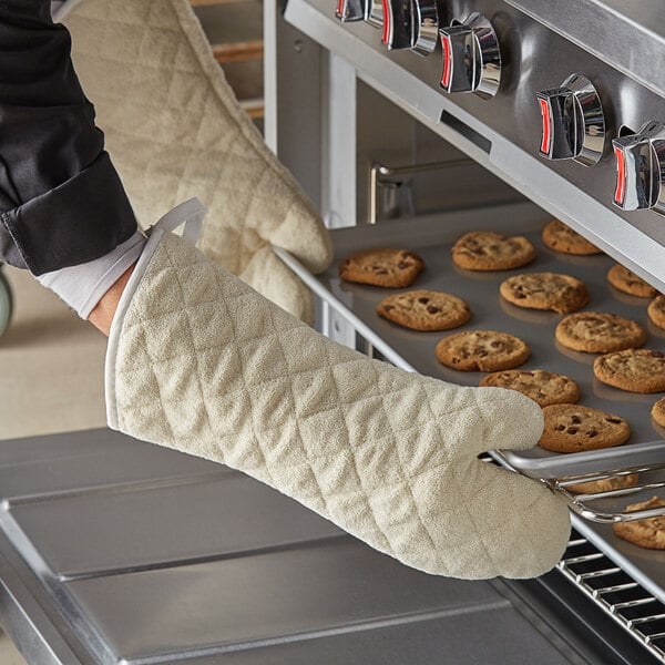 A person wearing Choice oven mitts takes cookies out of the oven.