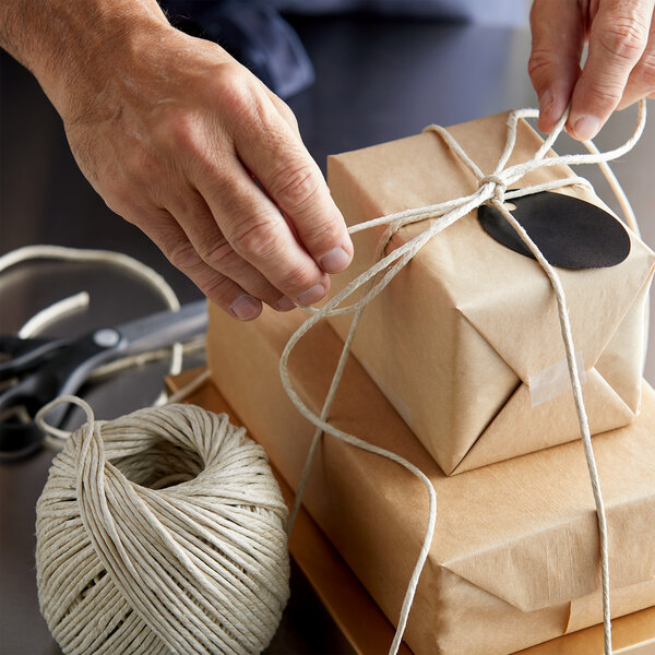 A person using 4-Ply Long-Fiber Hemp Spring Twine to tie a string on a box.