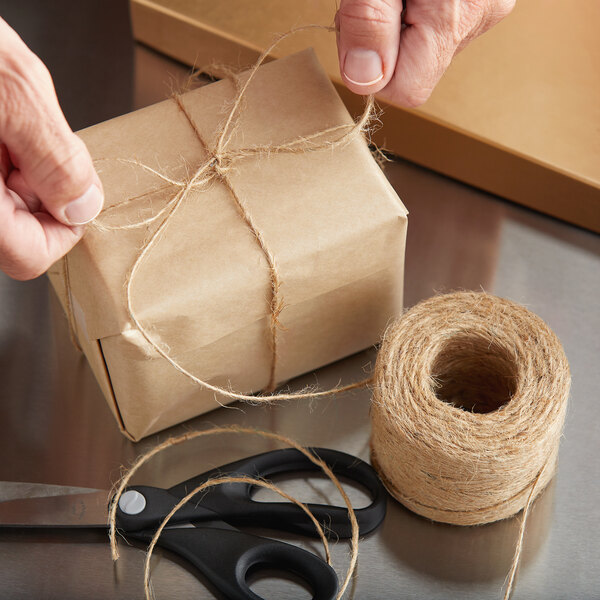 A person's hand tying 1-ply natural jute twine to a brown box.