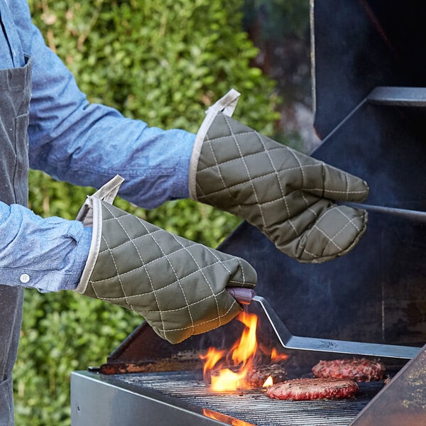 A man wearing Choice flame retardant oven mitts grilling meat.