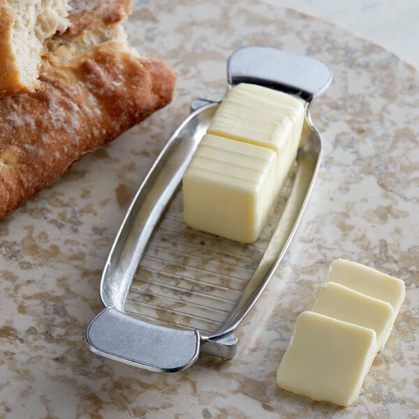 A piece of butter in a Fox Run aluminum butter slicer next to a piece of bread.