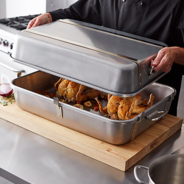 A man holding a Vollrath Wear-Ever aluminum double roaster pan with food inside.