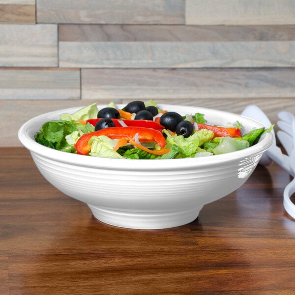 A Fiesta white china pedestal serving bowl filled with salad with olives and peppers.