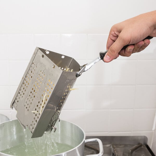 A hand using a Vollrath stainless steel pasta basket to remove pasta from a pot of water.