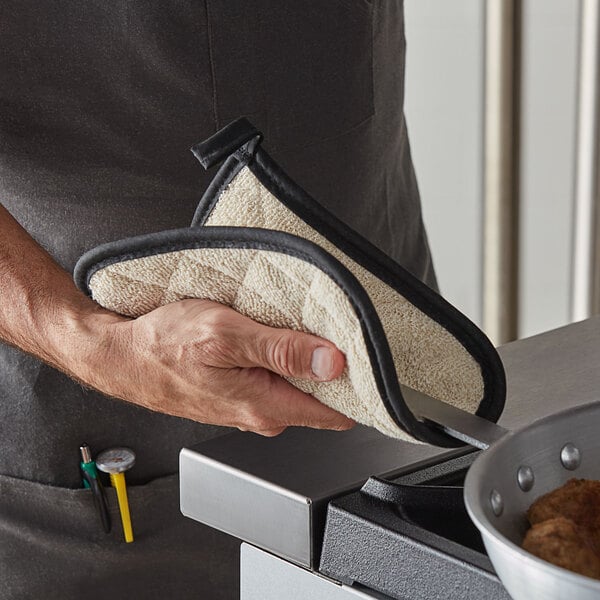 A person using a SafeMitt pot holder to hold a pan over a counter.
