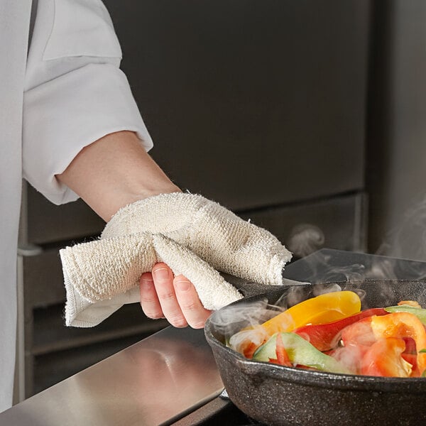 A person using a SafeMitt to grab a pan of food from the oven.