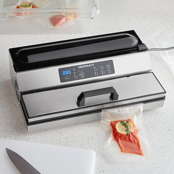 A VacPak-It stainless steel vacuum packaging machine on a white counter with buttons and a handle.