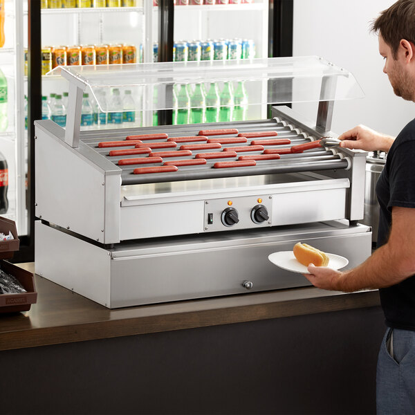 A man using an Avantco slanted hot dog roller grill to cook hot dogs.